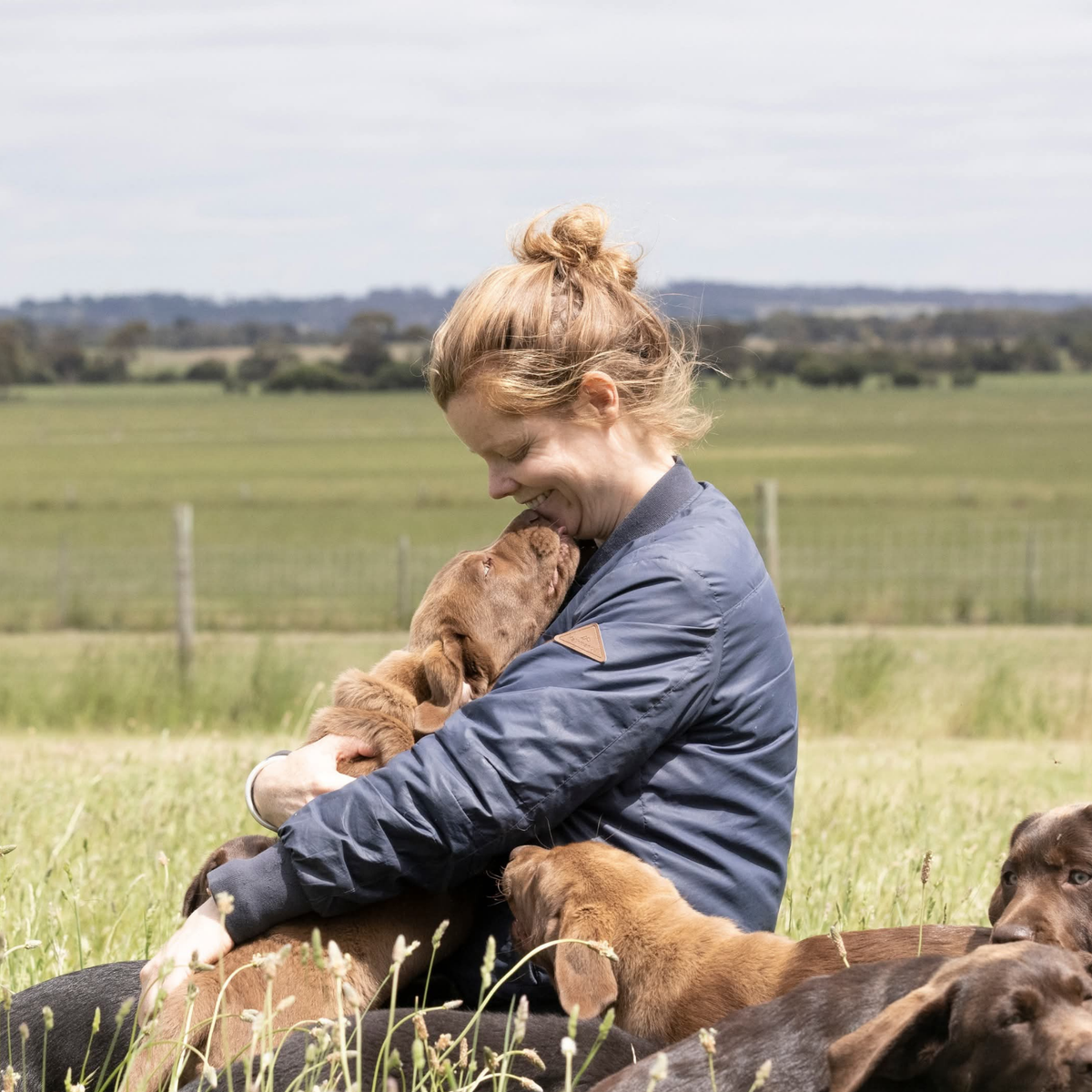Kristie, founder of Raw Spirit, sitting in a paddock holding one of her Labradors